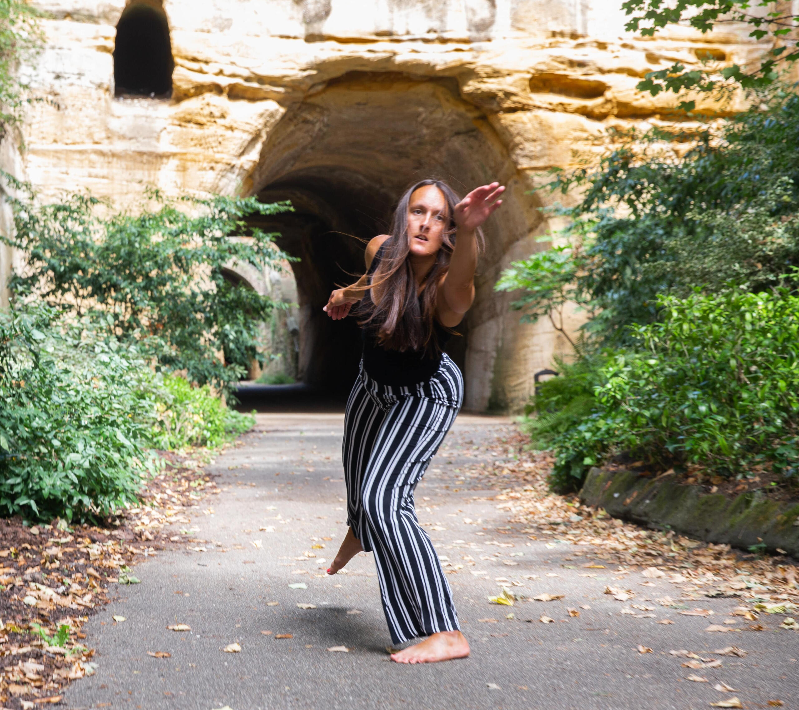 A dancer leaning sideways towards the camera outside in front of the entrance to a tunnel